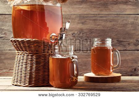 Fresh Homemade Kombucha Fermented Tea Drink In Jar With Faucet And In Cans-mugs On Wooden Background