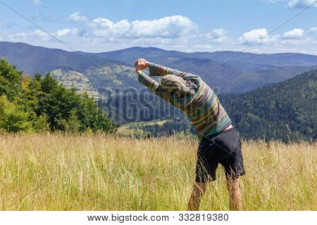 Back View Of Young Man In Green Hoodie, Exercising And Stretching Hands, Looking At Mountains Range,
