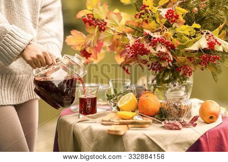 Autumn. A Table Set On The Banks Of The Lake Decorated With A Bouquet Of Autumn Leaves. Girl Pouring
