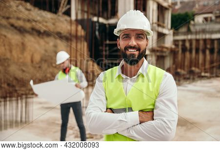 Positive Adult Bearded Ethnic Male Construction Engineer In Hardhats And Waistcoat Looking At Camera
