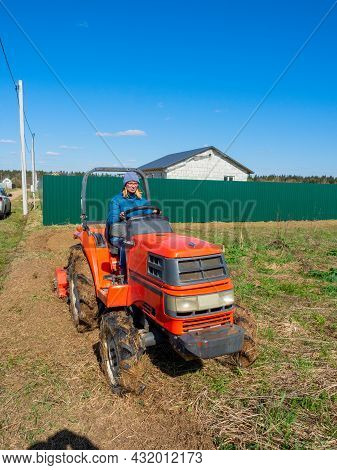 The Girl Sits In A Small Tractor And Drives Through The Field Mulching Grass. Land Cultivation, Agro