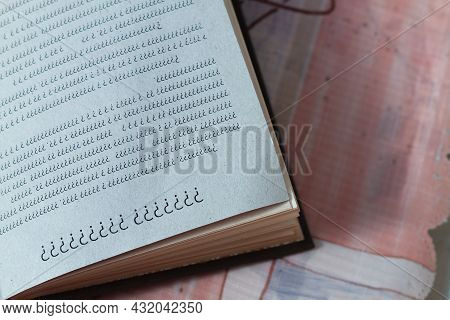 A Book With Incomprehensible Symbols In The Form Of Question Marks, Unreadable Text In The Book.