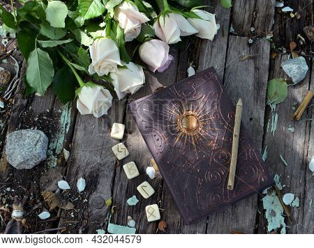 Top View Of Witch Grimoire Book, Runes And White Flowers On Planks Outside In The Garden. Esoteric, 