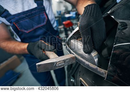 Repairman Peening Car Detail With Hammer In Workshop