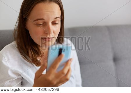 Closeup Portrait Of Sick Female Wearing White Shirt Looking At Smart Phone Display Very Close, Havin