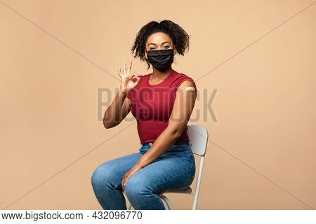 Young Afro Lady In Face Mask Showing Okay Gesture After Covid-19 Vaccine Injection, Recommending Cor