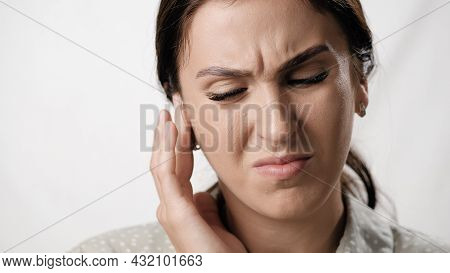 Earache. Suffering Woman On White Background With Emotions Of Pain On Her Face Touches Her Ear. Clos