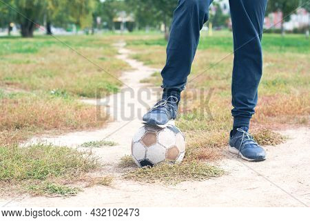 Old Soccer Ball With Teenager Feet On The Football Field. Selective Focus.