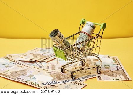 Buying Us Dollars In Uzbekistan. Us Dollars Roll In Shopping Trolley And Pile Of Uzbek Sums. Uzbek M