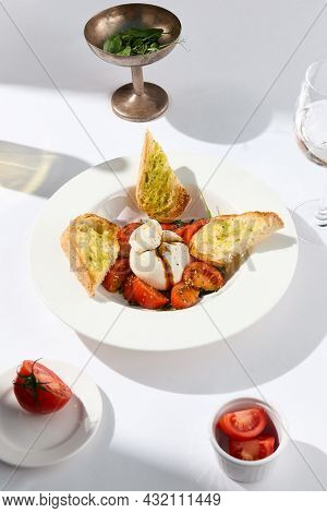 Traditional Italian salad with Burrata cheese and tomatoes. Fancy caprese with burrata cheese, cherry tomatoes, pesto and balsamic sauces. Summer dish with mozzarella cheese on white table with shadow