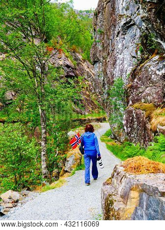 Tourist Woman With Norwegian Flag And Camera Walking Trough Mountains Path In Allmannajuvet Area Sau