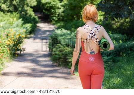 Kyiv, Ukraine 08.08.2021: Woman In Orange Yoga Jumpsuit With Her Back Turned Holding A Twisted Yogam