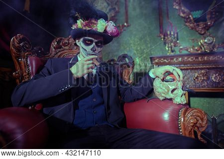 Dia de los muertos. Day of The Dead. The elegant and dangerous Baron Samedi smokes a cigar in a vintage castle. Handsome man with sugar skull makeup. Halloween.