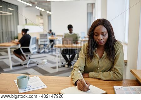 Pretty Serious Buisness Lady Sitting At Office Desk With Cup Of Coffee And Printed Reports And Takin