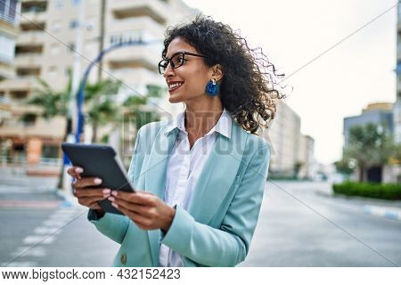 Young hispanic business woman wearing professional look smiling confident at the city using touchpad device