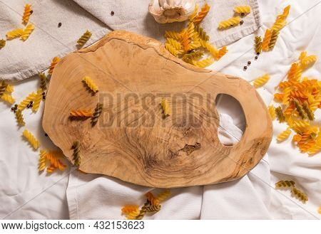 Cutting Board Curved Shape Of Olive Tree, Scattered Around Pasta, Garlic, Pepper. They Lie On A Crud