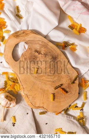 Cutting Board Curved Shape Of Olive Tree, Scattered Around Pasta, Garlic, Pepper. They Lie On A Crud
