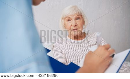 Blurred Geriatrician Writing Prescription Near Aged Woman