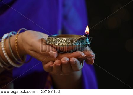 Woman Holding Lit Diya Lamp In Hands On Dark Background, Closeup. Diwali Celebration