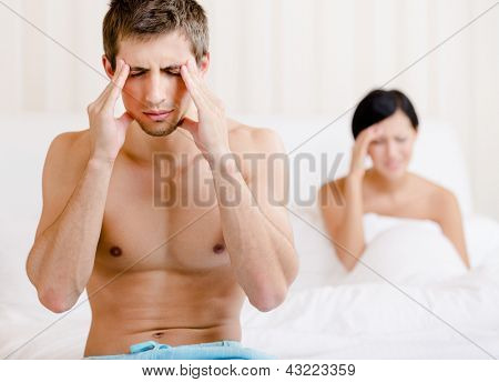 Junges Paar argumentiert im Bett. Deprimiert Mann sitzt auf dem Rand des Bettes. Mann im Fokus