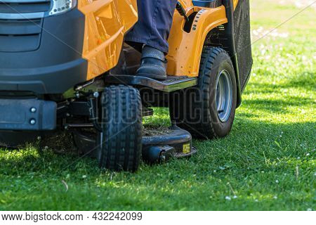 Gardener Driving A Riding Lawn Mower In A Garden , Cutting Grass, Closeup
