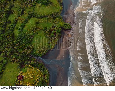 Aerial View Of Volcanic Sand Beach With River, Ocean And Waves In Balian, Bali