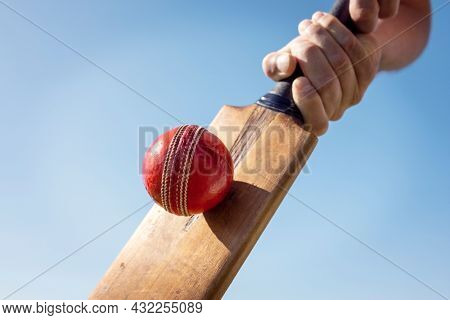 Cricket player batsman hitting a ball with a bat shot from below against a blue sky