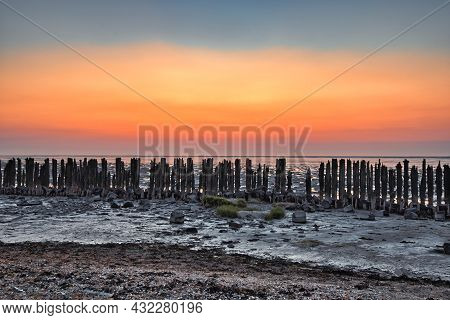 View Of The Wadden Sea During Sunset, At Low Tide. Wooden Posts As A Silhouette In The Mud. Unesco. 