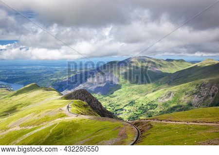 Railway track snaking up Mount Snowndon from Llanberis in the valley below. Snowdonia National Park, North Wales, UK, on a summer day. A popular tourist attraction for walking and hiking .