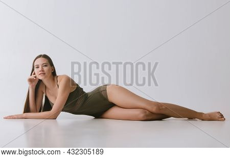 Full-lenghth Portrait Of Young Beautiful Woman In Green Underwear Lying On Floor Over Gray Backgroun