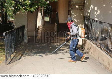 August 27, 2018 San Diego California: Gardner uses his High Power Backpack Air Blower to clean the sidewalk of dirt and leaves. 
