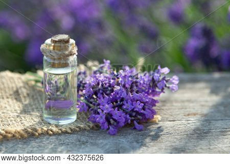 Glass bottle of Lavender essential oil on wood table and flowers field. Lavendula oleum