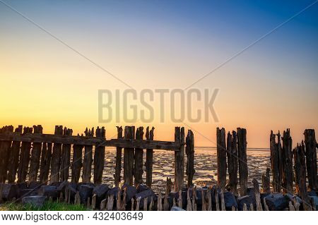 View Of The Wadden Sea During Sunset, At Low Tide. A Colorful Dramatic Sky. Wooden Posts As A Silhou