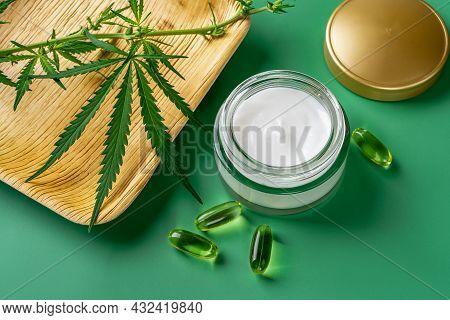 Anti-aging Face Cream, Few Cbd Oil Capcules And Cannabis Sativa Leaf Against Green Background. Moist