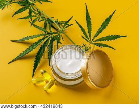Hemp Face Cream, Few Cbd Oil Capcules And And Green Cannabis Sativa Leaves Against Yellow Background