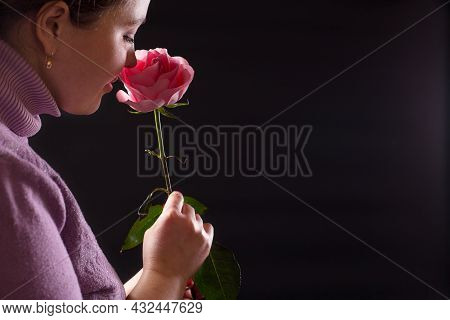 Sensual Young Girl Inhales The Delicate Scent Of A Pink Rose, On Black Background.