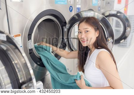 In The Self-service Laundry With Dryer Machines In The Backdrop, A Young Woman Enjoys Clean Ironed G