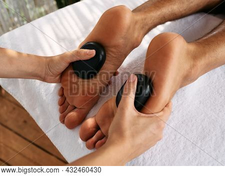 Hot Stone Foot Massage Therapy. Massage Therapist Doing Hot Stone Foot Massage For Mens Feet At Spa