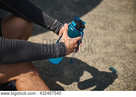 Close-up Of Male Athlete Hands Holding A Blue Bottle Full Of Fresh Water For Rehydrating After Heavy