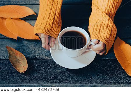 Hands In Yellow Knitted Sweater Holding A Cup Of Tea Among Fall Keaves, Autumn Concept