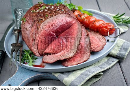 Modern style traditional barbecue haunch of venison sliced and as piece served with tomatoes and herbs as close-up on a Nordic design plate