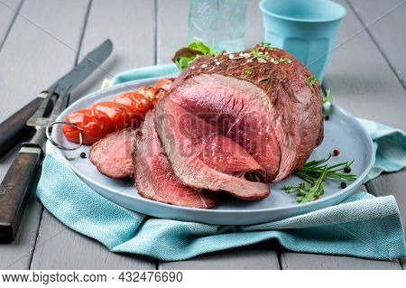 Modern style traditional barbecue haunch of venison sliced and as piece served with tomatoes and herbs as close-up on a Nordic design plate