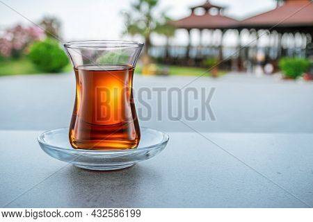 Turkish tea served in tulip-shaped glass on a small saucer blurred nature background. Summer holiday background.
