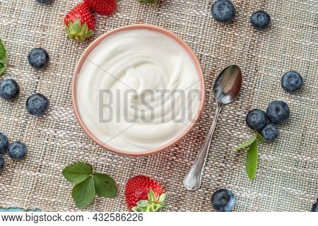 Ceramic bowl with plain yoghurt and berries on the table. Light summer mood.