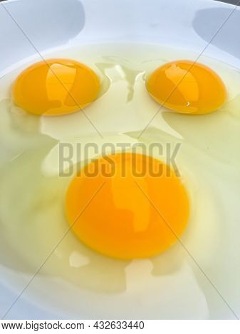 Three bright yellow raw chicken eggs in a white bowl.