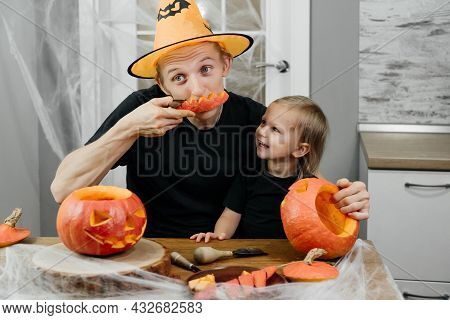 Parent With Chld Are Carving Jack O Lantern From Pumpkin For Halloween At Home. Father In Hat Prepar