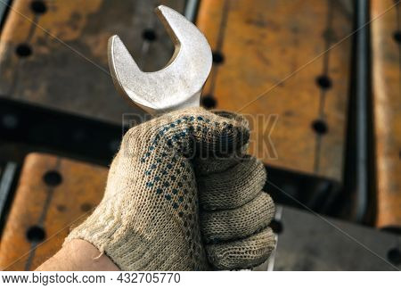 Fork Wrench Clenched Into A Worker's Fist Against A Background Of Rusty, Metal Parts. The Hand Of A 