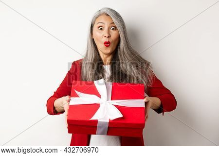 Surprised Asian Senior Woman Receiving Present On Mother Day, Holding Red Box With Gift And Looking 