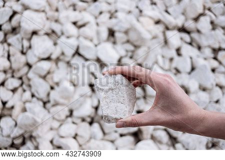 Hand Holds A White Chalkstone With A Lot Of Stones On The Background