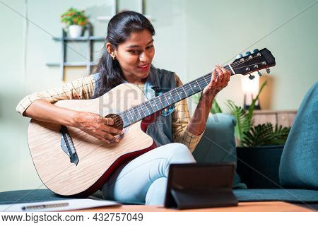 Young Girl Learning To Play Acoustic Guitar At Home From Digital Tablet Through Video Call - Concept